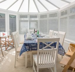 A dining area in a conservatory with a table set for eight and a high chair at Rock Point in Salcombe