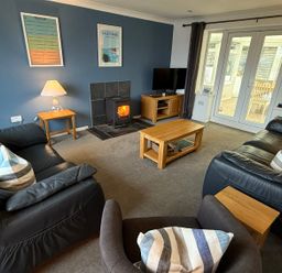 A living room with two sofas an armchair a coffee table a side table a wood stove a television and glass doors at Rock Point in Salcombe