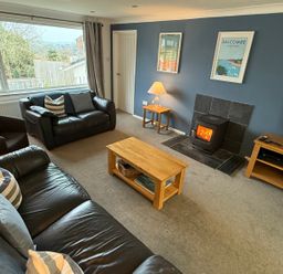 A living room with black leather sofas wooden coffee tables a lit fireplace and a television at Rock Point in Salcombe