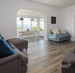 A living room with sofas and a dining area with a table and chairs by a window showing an outdoor view at Seaspray Bigbury-on-Sea