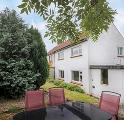 An outdoor seating area with a black table and red chairs next to a white two-story house with trees and grass at 7 Dale End in Danby near Castleton