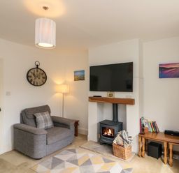 A living room with an armchair a wall clock a wood stove and a TV at 7 Dale End in Danby near Castleton