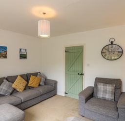 A living room with gray sofas and a green door with wall clock at 7 Dale End in Danby near Castleton