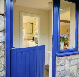 A blue half door leading to a kitchen with white cabinets and a window at The Hideaway in Eckington