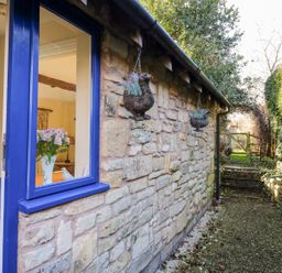 A stone exterior wall with a blue door and window two hanging bird planters a gravel path and garden gate at The Hideaway in Eckington