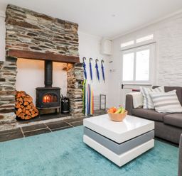 A living room with a stone fireplace a gray sofa striped cushions a modern white coffee table with fruit and a blue rug at Rock House Trebarwith Strand near Tintagel