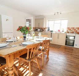 A kitchen with a wooden dining table set with plates and glasses and white cabinets at Stone Wheel Cottage in Hook Norton