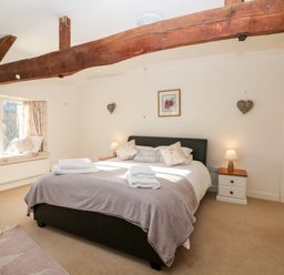 A bedroom with a bed window seat bedside tables and wooden ceiling beam at Stone Wheel Cottage in Hook Norton