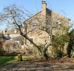 A stone house with a glass conservatory and leafless trees in a garden at Stone Wheel Cottage in Hook Norton