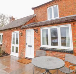 A patio with a round metal table and two chairs outside a red brick house at Wigrams Canalside Cottage in Napton-on-the-Hill