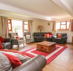 A living room with leather sofas plaid armchairs a wooden chest coffee table a red and white rug and a television at Treboeth in Knighton