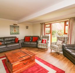 A living room with leather sofas plaid armchairs a wooden coffee table and a sliding door to a garden at Treboeth in Knighton