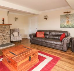 A living room with a brown leather sofa and armchair a wooden chest coffee table a stone fireplace and a painting of a rabbit at Treboeth in Knighton