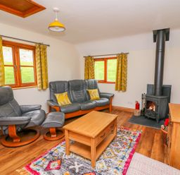 A living room with leather sofa and armchair wooden coffee table wood-burning stove and patterned rug at Pines Pitch in Knighton