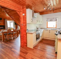 A kitchen with white cabinets and granite countertops next to a dining area with a wooden table and chairs at Pines Pitch in Knighton
