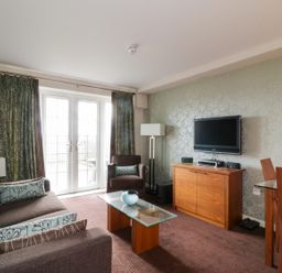 A living room with a sofa armchair glass coffee table and TV on a cabinet at Ullswater 29 in Penrith