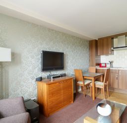 A living area with a sofa lamp television wooden cabinet dining table chairs and a kitchen with wooden cabinets at Ullswater 29 in Penrith