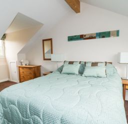 A bedroom with a bed covered by a green cover and pillows two bedside tables with lamps and a wooden chest of drawers and a window at Ullswater 29 in Penrith