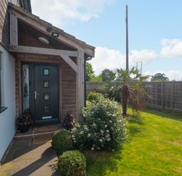 Front door entrance with plants and bushes beside a lawn with a wooden fence at Longmynd in Gloucester