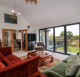 A living room with red and green sofas a wooden coffee table a gray armchair a television and large glass doors overlooking a garden at Longmynd in Gloucester