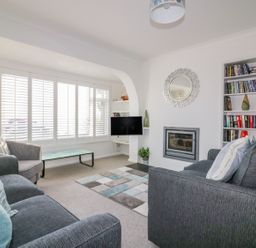 A living room with sofas a coffee table a rug a built in bookshelf and a wall mounted tv at Bayview in Mevagissey