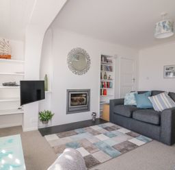 A living room with a grey sofa a rug and a fireplace at Bayview in Mevagissey