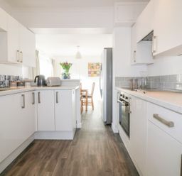A kitchen with white cabinets a gray countertop a black kettle a toaster and flowers on the counter at Bayview in Mevagissey