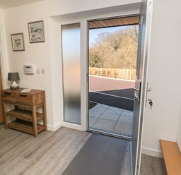 An entryway with an open door showing an outdoor area a wooden console table with a lamp and two pictures on the wall at High Tide House in Craster