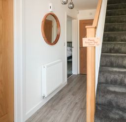 A hallway with wooden doors a grey carpeted staircase a round mirror and a radiator at High Tide House in Craster
