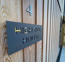 A wooden exterior wall with a metal sign reading High Tide House and the number 4 near a wooden gate at High Tide House in Craster