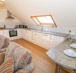 A kitchen with white cabinets a countertop window and a small dining area with set tableware at Llain Haf in Llangefni