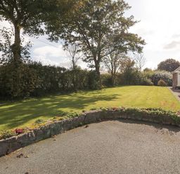 A garden with trees grass and a stone wall next to a stone house at Llain Haf in Llangefni