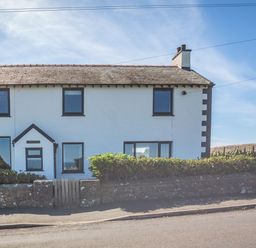 A two-story white house with dark window frames a hedge and a stone wall with a wooden gate at Tyn Y Berth in Benllech