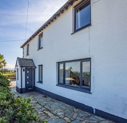 The exterior of a white house with multiple windows a dark door and a stone pathway with plants nearby at Tyn Y Berth in Benllech