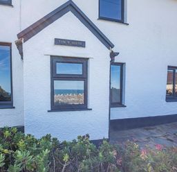The exterior of a white building with multiple windows and plants in front at Tyn Y Berth in Benllech