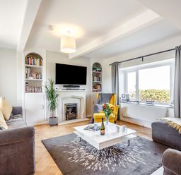 A living room with sofas a yellow armchair a white coffee table and a fireplace at Tyn Y Berth in Benllech