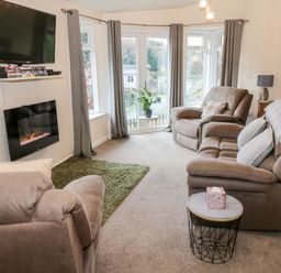 A living room with armchairs sofas a television and an electric fireplace at The Wee Lodge in Dollar