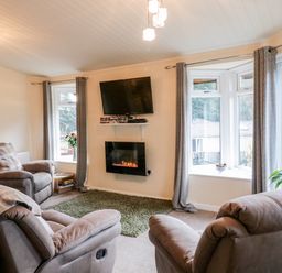 A living room with two armchairs a wall mounted TV an electric fireplace and large windows at The Wee Lodge in Dollar