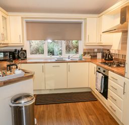 A kitchen with wooden countertops white cabinets a gas stove microwave coffee maker and window with a blind at The Wee Lodge in Dollar