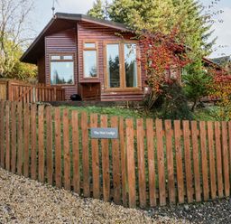 A wooden cabin with large windows and a wooden fence labeled The Wee Lodge in Dollar