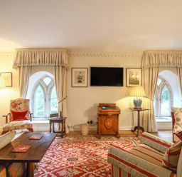 A living room with floral and striped armchairs a wooden coffee table a patterned rug and a wall-mounted TV at All Souls Cottage in Eastleach Cotswolds