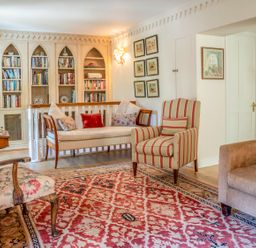 A sitting room with patterned armchairs a sofa built in bookcases and a red patterned rug at All Souls Cottage in Eastleach Cotswolds