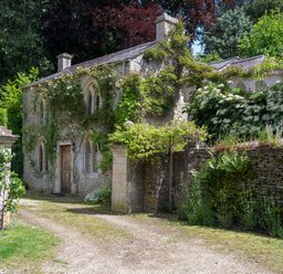 A stone cottage with climbing plants and bushes around a driveway at All Souls Cottage in Eastleach Cotswolds