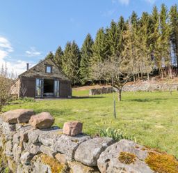 A stone barn with open wooden doors in a grassy yard with trees and a stone wall at Thompson Rigg Barn in Langdale End near Thornton Dale
