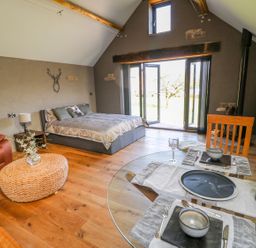 A bedroom with a bed a leather armchair a wicker ottoman a dining table and glass doors at Thompson Rigg Barn Langdale End near Thornton Dale