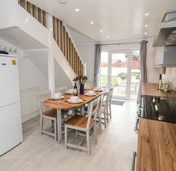 A kitchen dining area with a wooden table set for six and a staircase along the wall at Ty Gilbert in Benllech