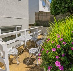 A small outdoor patio with white metal table and chairs next to a white building with windows and purple flowers at 1 Lyndhurst in Salcombe