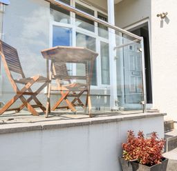 A small outdoor patio with two wooden chairs a table glass railing potted plant and a door at 1 Lyndhurst in Salcombe