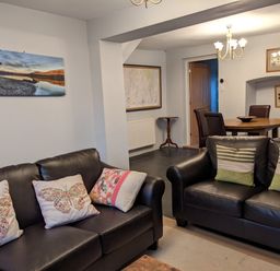 A living room with two black leather sofas and a dining area with round table and four chairs at Rose Cottage in Lowick Bridge