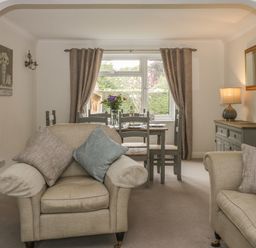 A living room with beige armchairs and a dining table with chairs by a window with curtains at Humble Bee Cottage in Wold Newton near Hunmanby